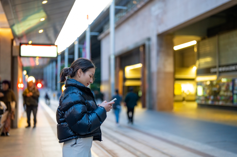 駅でスマホの交通アプリを見ながらトラムを待つ様子